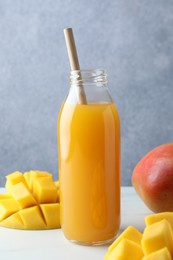 Photo of Tasty mango juice in glass bottle and fresh fruits on white table