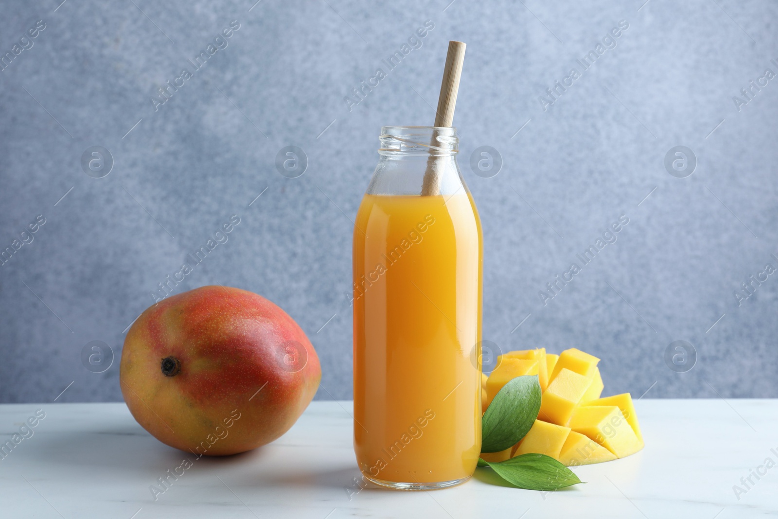 Tasty mango juice in glass bottle, fresh fruits and green leaves on white marble table Photo of Tasty mango juice in glass bottle, fresh fruits and green leaves on white marble table