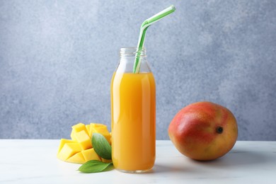 Photo of Tasty mango juice in glass bottle, fresh fruits and green leaves on white marble table