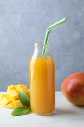 Photo of Tasty mango juice in glass bottle, fresh fruits and green leaves on white marble table