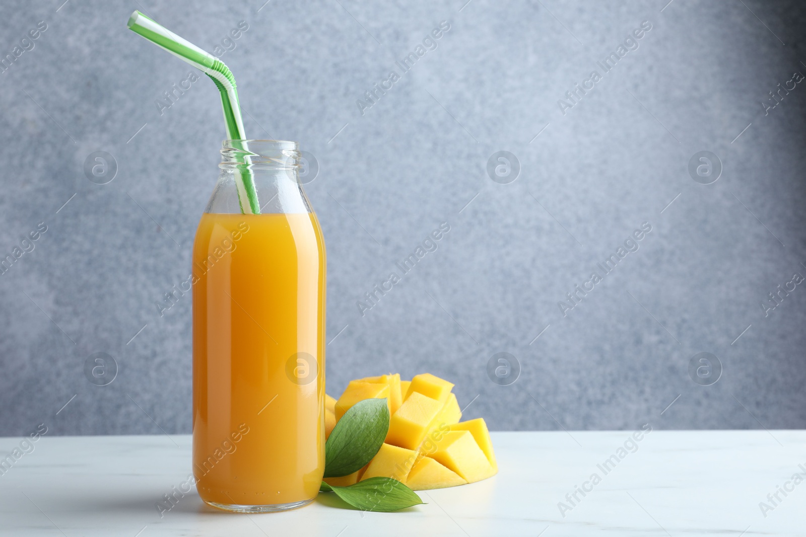 Tasty mango juice in glass bottle, fresh fruit and green leaves on white marble table, space for text Photo of Tasty mango juice in glass bottle, fresh fruit and green leaves on white marble table, space for text