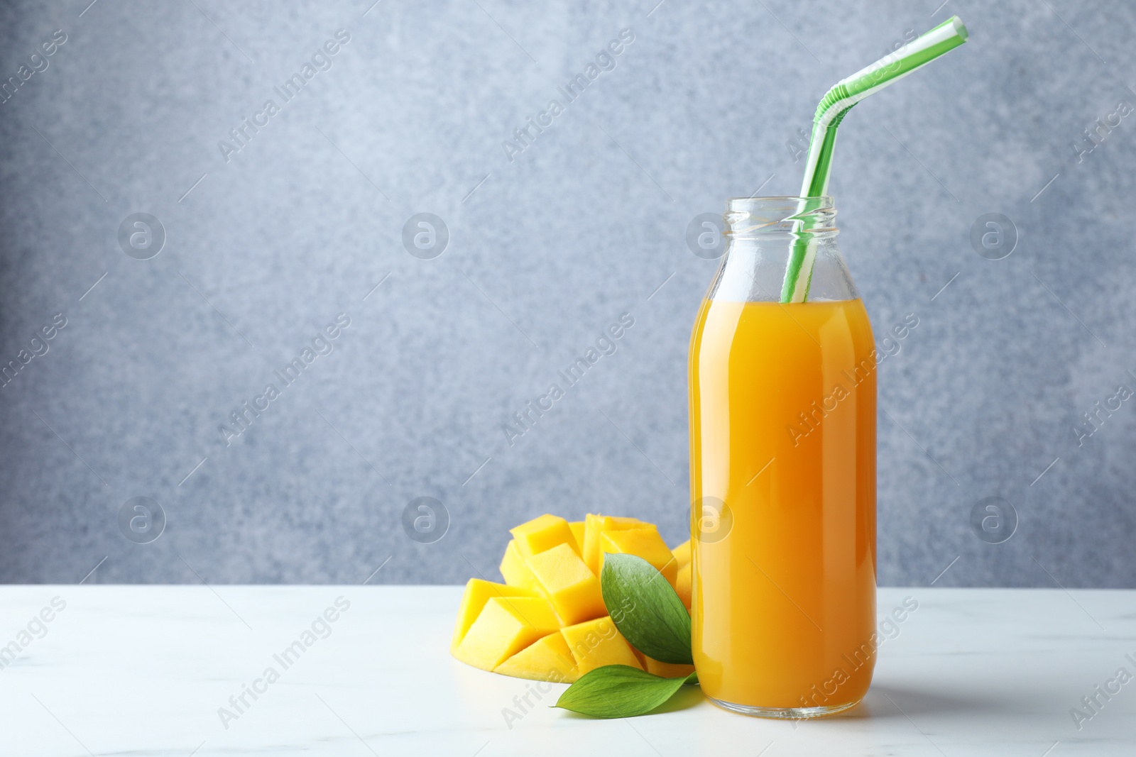 Tasty mango juice in glass bottle, fresh fruit and green leaves on white marble table, space for text Photo of Tasty mango juice in glass bottle, fresh fruit and green leaves on white marble table, space for text