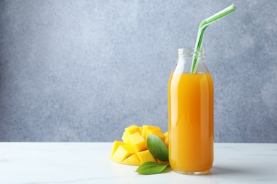 Photo of Tasty mango juice in glass bottle, fresh fruit and green leaves on white marble table, space for text