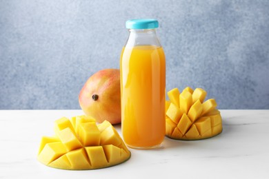 Photo of Tasty mango juice in glass bottle and fresh fruits on white marble table
