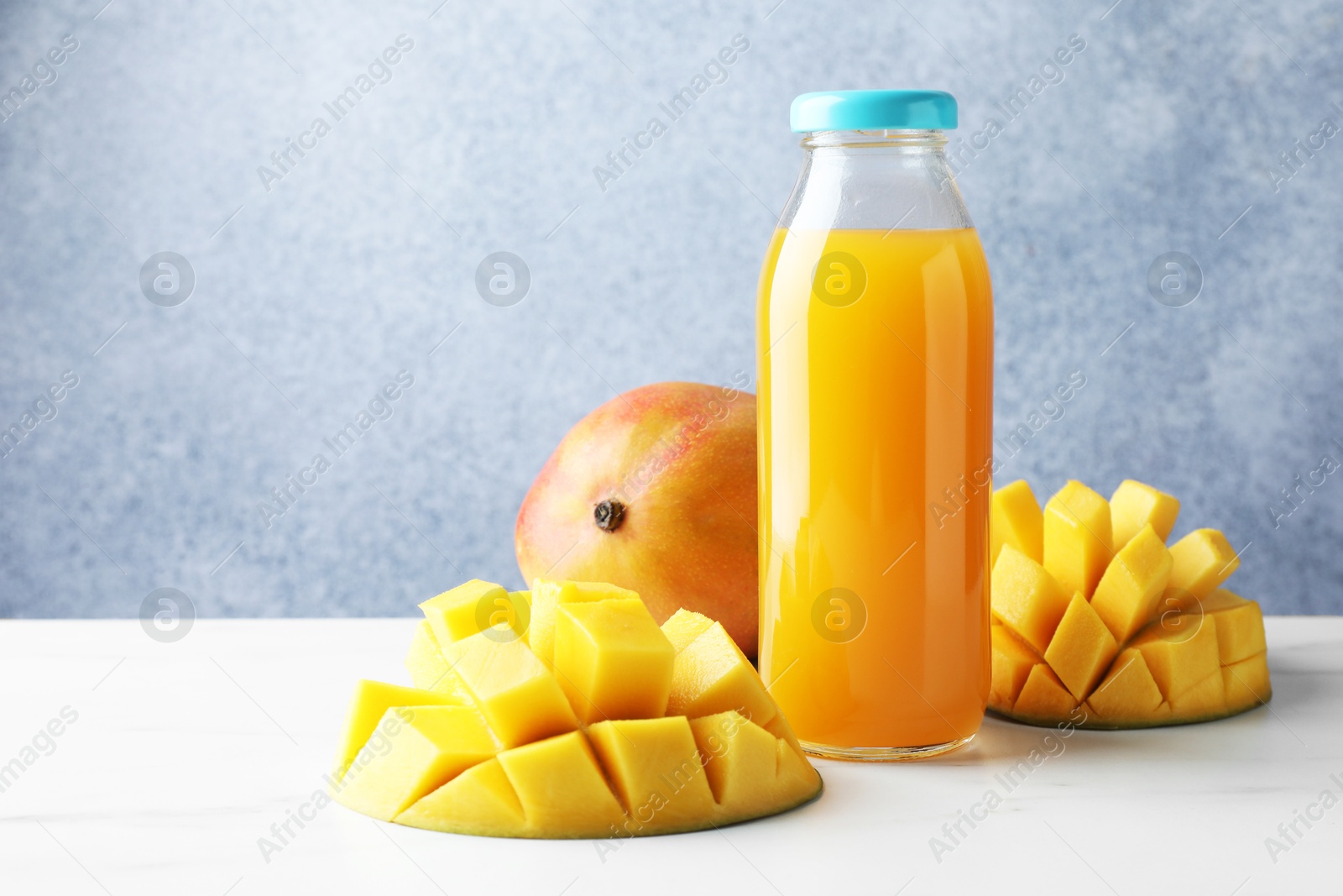 Tasty mango juice in glass bottle and fresh fruits on white marble table Photo of Tasty mango juice in glass bottle and fresh fruits on white marble table