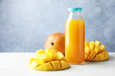 Photo of Tasty mango juice in glass bottle and fresh fruits on white marble table