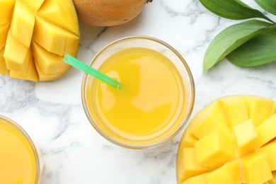 Photo of Tasty mango juice in glass, fresh fruits and green leaves on white marble table, flat lay
