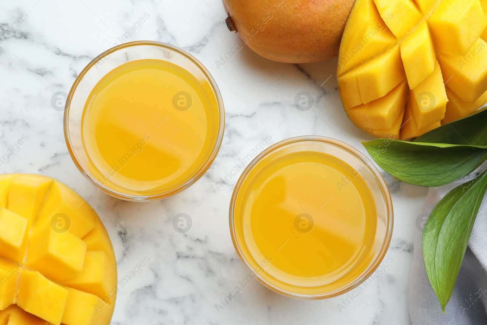 Tasty mango juice in glasses, fresh fruits and green leaves on white marble table, flat lay Photo of Tasty mango juice in glasses, fresh fruits and green leaves on white marble table, flat lay