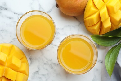 Photo of Tasty mango juice in glasses, fresh fruits and green leaves on white marble table, flat lay