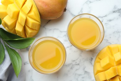 Photo of Tasty mango juice in glasses, fresh fruits and green leaves on white marble table, flat lay