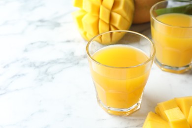 Photo of Tasty mango juice in glasses and fresh fruits on white marble table, closeup. Space for text