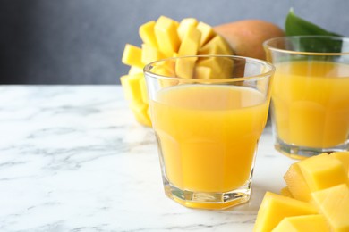 Photo of Tasty mango juice in glasses and fresh fruits on white marble table, closeup. Space for text