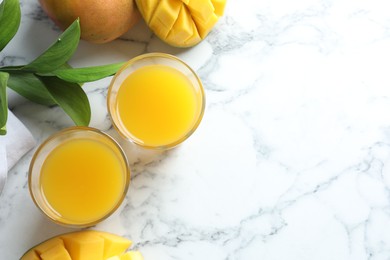 Photo of Tasty mango juice in glasses, fresh fruits and leaves on white marble table, flat lay. Space for text