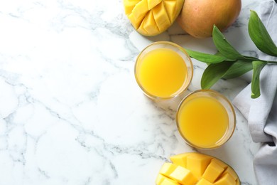 Photo of Tasty mango juice in glasses, fresh fruits and leaves on white marble table, flat lay. Space for text