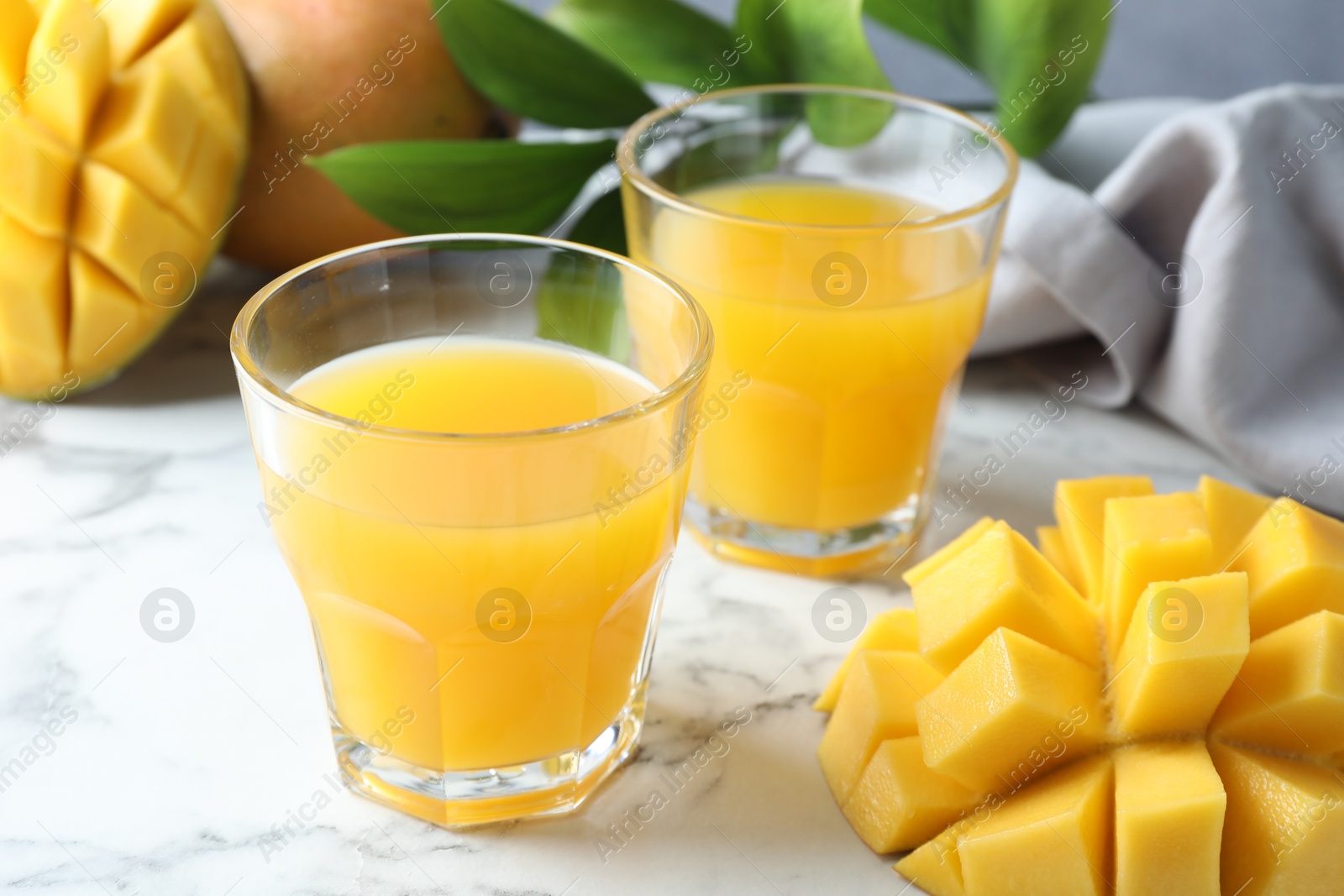 Tasty mango juice in glasses, fresh fruits and green leaves on white marble table, closeup Photo of Tasty mango juice in glasses, fresh fruits and green leaves on white marble table, closeup