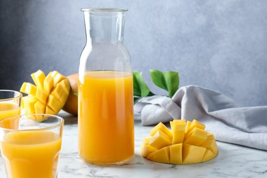 Photo of Tasty mango juice, fresh fruits and green leaves on white marble table