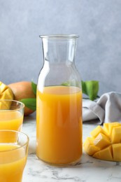 Photo of Tasty mango juice, fresh fruits and green leaves on white marble table