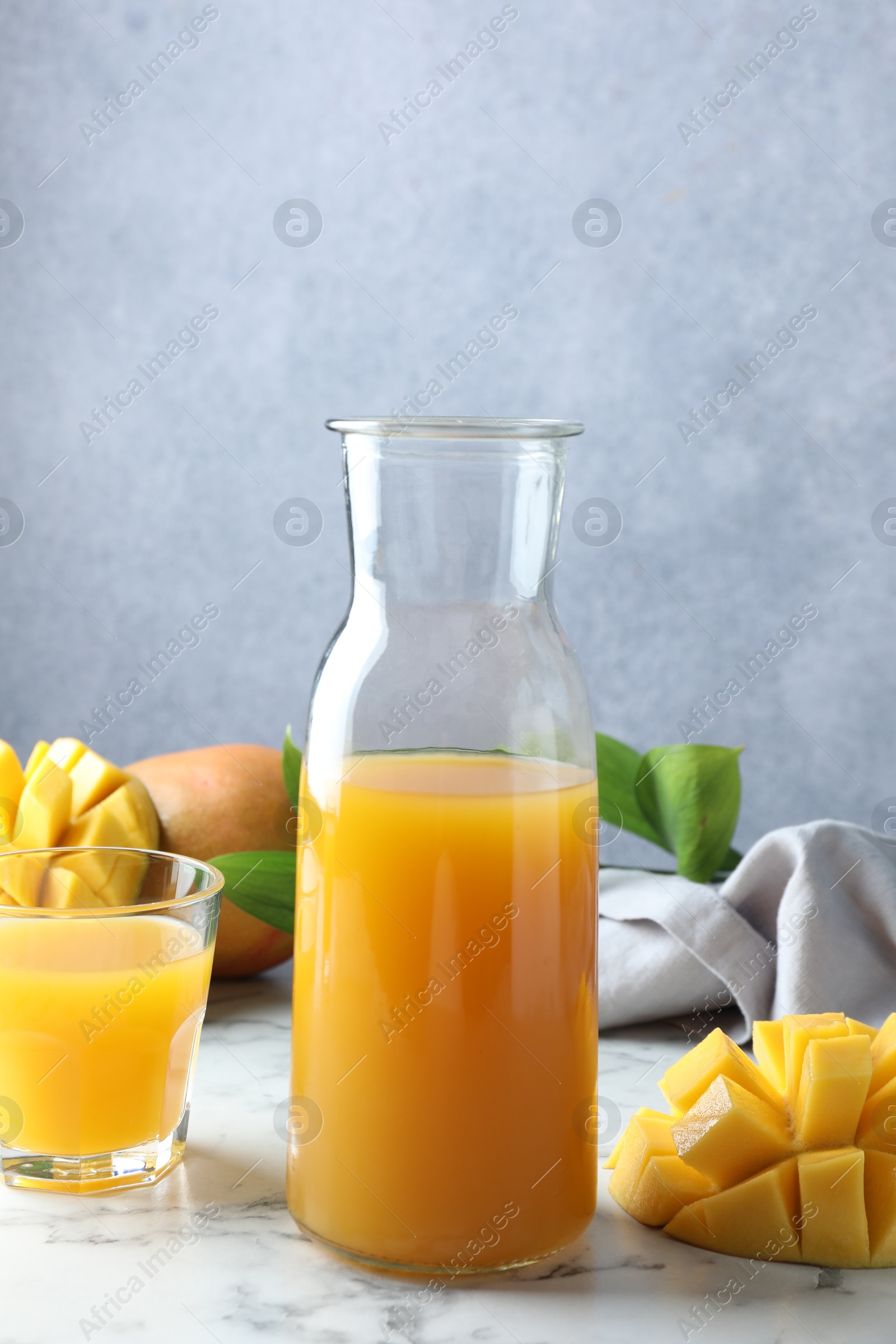 Tasty mango juice, fresh fruits and green leaves on white marble table Photo of Tasty mango juice, fresh fruits and green leaves on white marble table
