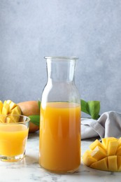 Photo of Tasty mango juice, fresh fruits and green leaves on white marble table