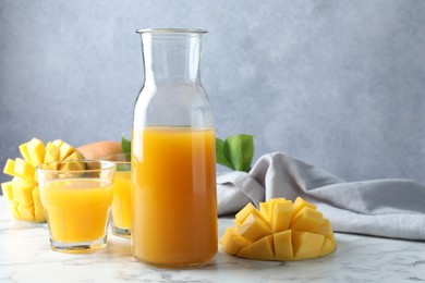 Photo of Tasty mango juice, fresh fruits and green leaves on white marble table