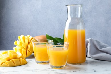 Photo of Tasty mango juice, fresh fruits and green leaves on white marble table