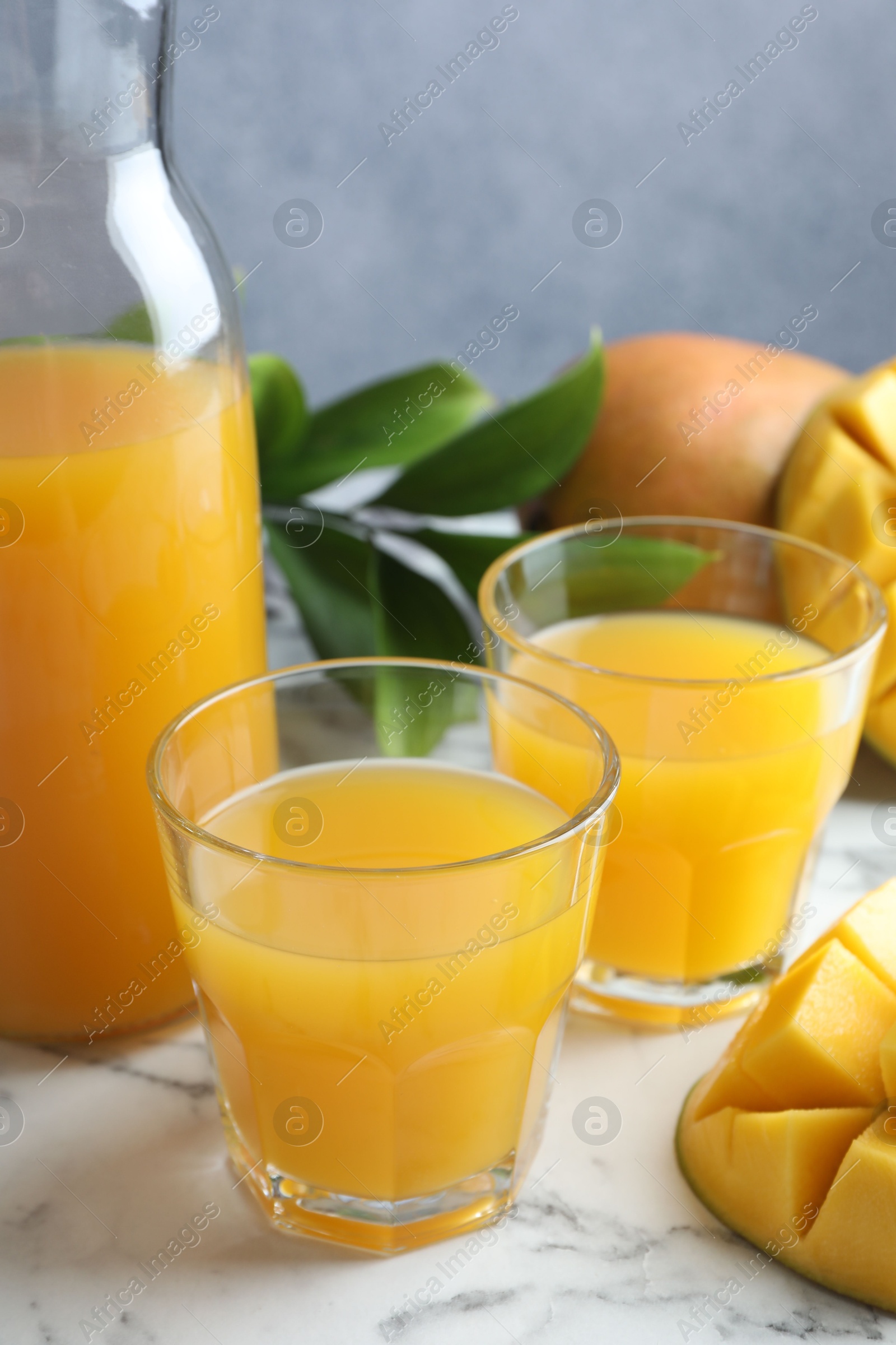 Tasty mango juice in glasses, fresh fruits and green leaves on white marble table, closeup Photo of Tasty mango juice in glasses, fresh fruits and green leaves on white marble table, closeup