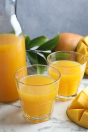 Photo of Tasty mango juice in glasses, fresh fruits and green leaves on white marble table, closeup