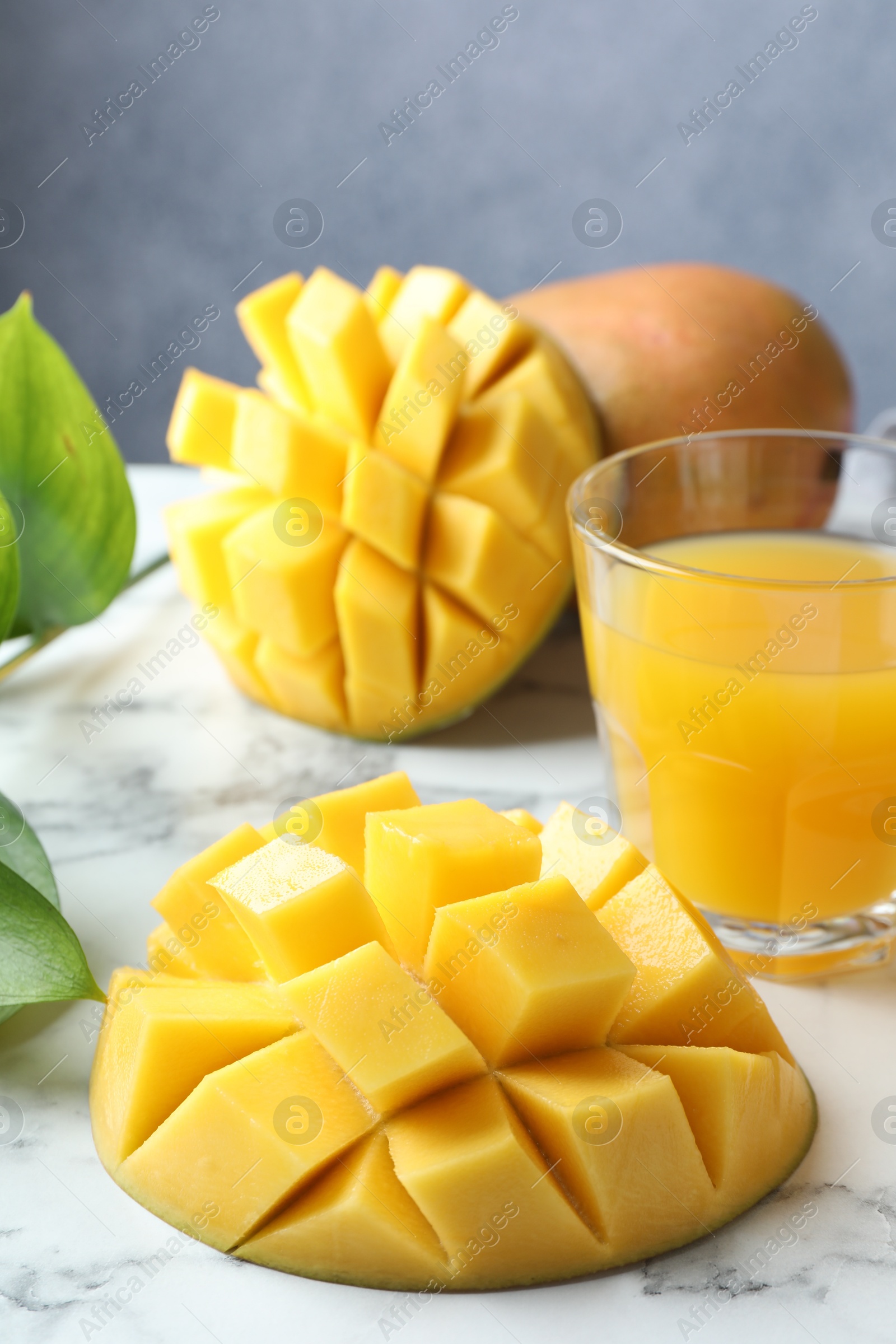 Tasty mango juice in glass, fresh fruits and green leaves on white marble table, closeup Photo of Tasty mango juice in glass, fresh fruits and green leaves on white marble table, closeup