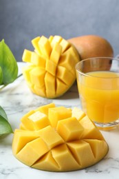 Photo of Tasty mango juice in glass, fresh fruits and green leaves on white marble table, closeup