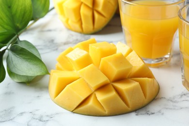 Photo of Tasty mango juice, fresh fruits and green leaves on white marble table, closeup
