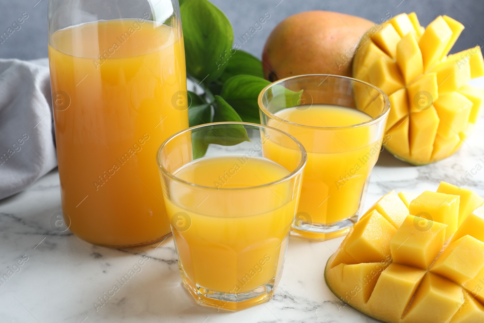 Tasty mango juice in glasses, fresh fruits and green leaves on white marble table, closeup Photo of Tasty mango juice in glasses, fresh fruits and green leaves on white marble table, closeup