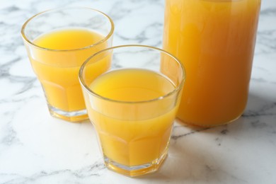 Photo of Tasty mango juice in glasses and carafe on white marble table, closeup
