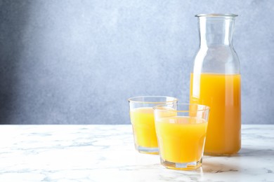 Photo of Tasty mango juice in glasses and carafe on white marble table, space for text