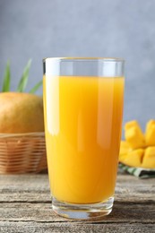 Photo of Tasty mango juice in glass and fresh fruits on wooden table, closeup
