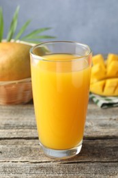 Photo of Tasty mango juice in glass and fresh fruits on wooden table, closeup