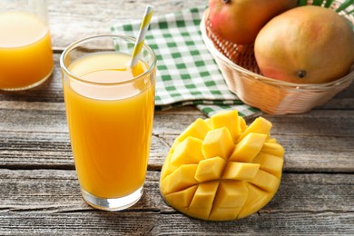 Photo of Tasty mango juice in glass and fresh fruits on wooden table, closeup