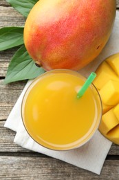 Photo of Tasty mango juice in glass, fresh fruits and green leaves on wooden table, flat lay