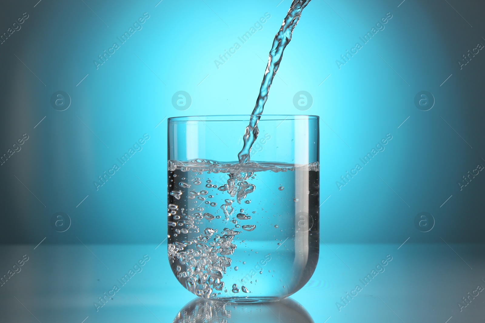 Pouring water into glass on mirror table against light blue gradient background. Backlit Photo of Pouring water into glass on mirror table against light blue gradient background. Backlit