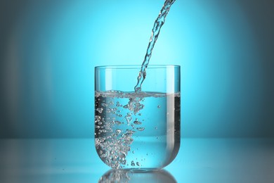 Photo of Pouring water into glass on mirror table against light blue gradient background. Backlit