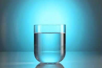 Photo of Fresh water in glass on mirror table against light blue gradient background. Backlit