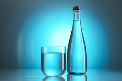 Photo of Fresh water in glass and bottle on mirror table against light blue gradient background. Backlit