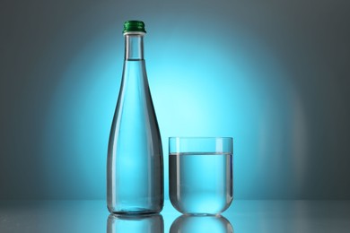 Photo of Fresh water in glass and bottle on mirror table against light blue gradient background. Backlit