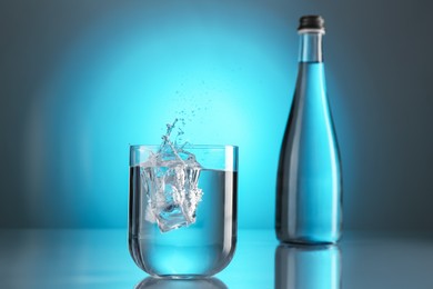 Photo of Fresh water splashing out of glass on mirror table against light blue gradient background. Backlit