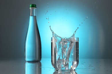 Photo of Fresh water splashing out of glass on mirror table against light blue gradient background. Backlit