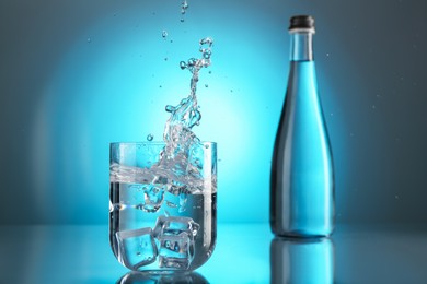 Photo of Fresh water splashing out of glass on mirror table against light blue gradient background. Backlit