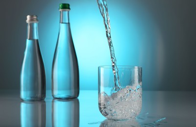 Photo of Pouring water into glass on mirror table against light blue gradient background. Backlit