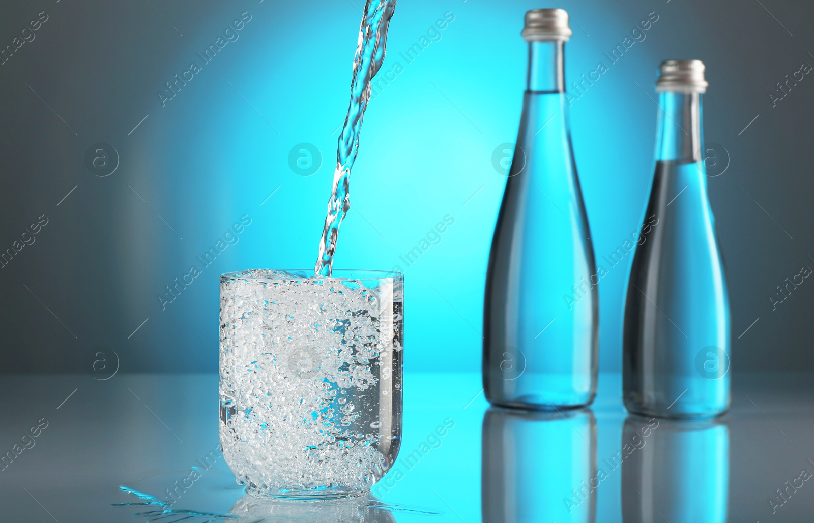 Pouring water into glass on mirror table against light blue gradient background. Backlit Photo of Pouring water into glass on mirror table against light blue gradient background. Backlit