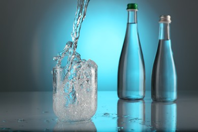 Photo of Pouring water into glass on mirror table against light blue gradient background. Backlit