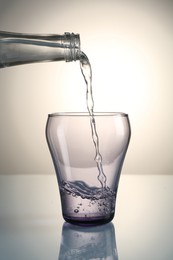 Photo of Pouring water from bottle into glass on mirror table against gray gradient background