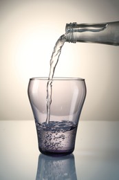 Photo of Pouring water from bottle into glass on mirror table against gray gradient background